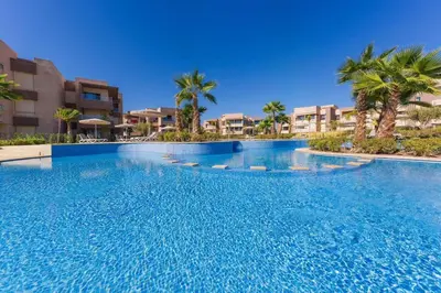 a large swimming pool with palm trees and buildings at Spacious 2BR , Pool & Garden , Golf View , Fast WiFi in Marrakech
