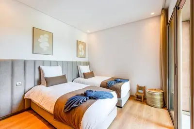 two beds in a room with white walls and wood floors at Spacious 2BR , Pool & Garden , Golf View , Fast WiFi in Marrakech