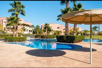 a swimming pool with an umbrella and palm trees at Appartement 2 chambres a PRESTIGIA piscine in Marrakech