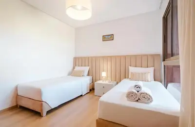 two beds in a bedroom with white walls and wood floors at Appartement 2 chambres a PRESTIGIA piscine in Marrakech