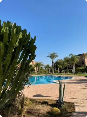 a swimming pool with a cactus in the foreground at Welcome to your Stylish Atlas View Apartment in Marrakech