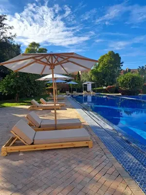 a group of lounge chairs with an umbrella next to a swimming pool at Chic Palm Grove Apartment Pool View in Marrakech
