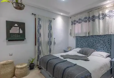 a bedroom with a bed with a blue headboard and curtains at Dar Choway Ground Floor Apartment in Marrakech