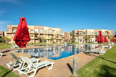 a pool with chairs and umbrellas in front of a building at The Calm Haven - Marrakech - Prestigia in Marrakech