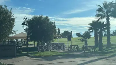 a park with benches and palm trees and a sign at Appartement Ksour in Sraghna