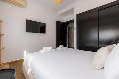 a white bedroom with a large white bed and a tv at One bedroom studio in Guéliz, pool & gym in Marrakech