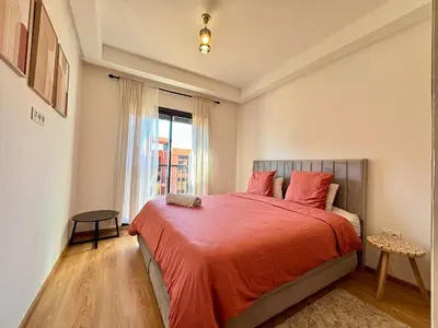 a bedroom with a bed with a red comforter and a window at Cosy appartement , Marrakech Noria golf in Marrakech