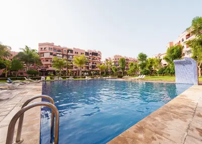 a swimming pool with chairs and buildings in the background at New 2BR Apartment in Marrakech with Pools, Gym, Security & Terrace in Marrakech