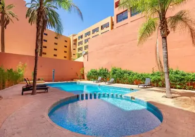 a swimming pool with palm trees and a building at Andalous Prestige in Marrakech