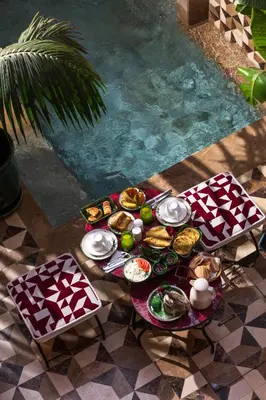 a table with plates of food next to a pool at Riad Dar Shala in Marrakech