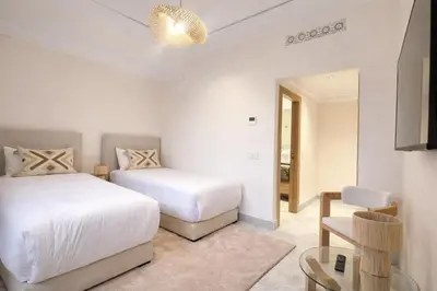 a white bedroom with two beds and a table at Luxury 2 Bedroom Apartment Pool & Garden Wifi in Marrakech