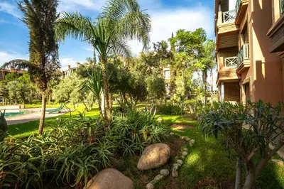 a garden in front of a building with trees and a pool at Appartement de charme avec piscine a Marrakech in Marrakech