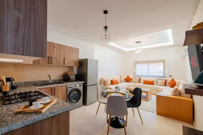 a kitchen and living room with a table and chairs at 1BR Cosy 2 min M Avenue Parking, Piscine & Fibre in Marrakech