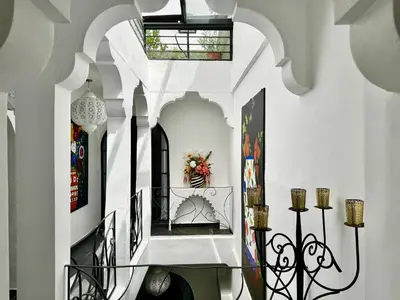 a hallway with white walls and a staircase with art at Riad Florival breakfast private kasbah in Marrakech