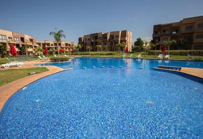 a large blue swimming pool with chairs and buildings at Premium Apartment in Marrakech Argan Golf Residence with pool & WiFi in Marrakech