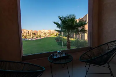 a window with two chairs and a table and a palm tree at Premium Apartment in Marrakech Argan Golf Residence with pool & WiFi in Marrakech