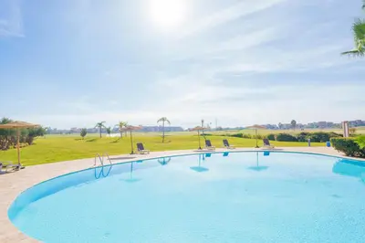 a large swimming pool with chairs and a field at Stylish Flat, Pool, Garden & Fast Wi-Fi in Marrakech