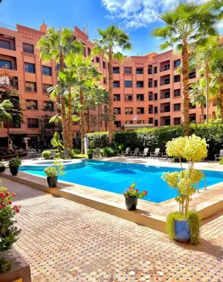 a swimming pool in front of a building with palm trees at Caprice Palace Residence Bella Anima in Marrakech