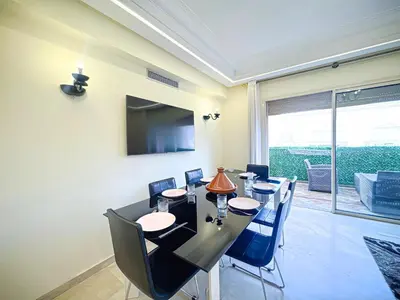 a dining room with a table and chairs and a television at Confort Signature - Piscine, balcon & parking in Marrakech