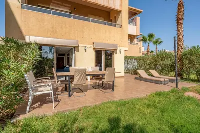 a wooden deck with chairs and a table in front of a house at Sunny Getaway with Pool Access & Private Yard in Marrakech