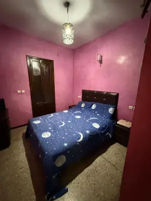 a bedroom with a bed with a blue comforter and pink walls at Location longue durée in Marrakech