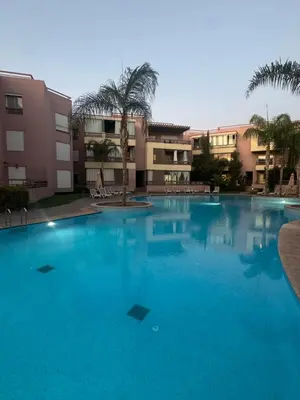 a large blue swimming pool with palm trees and buildings at Appartement moderne avec terrasse vue piscine in Marrakech