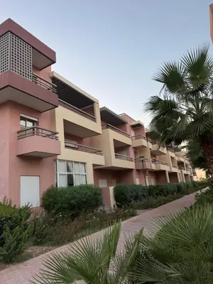 a pink building with a palm tree in front of it at Appartement moderne avec terrasse vue piscine in Marrakech