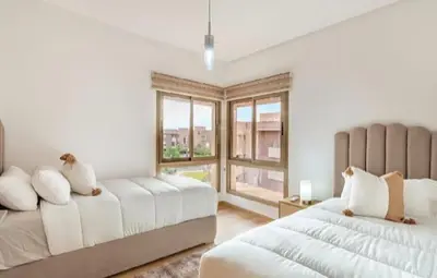 a white bedroom with two beds and a window at Prestigia Golf Resort Luxury in Marrakech