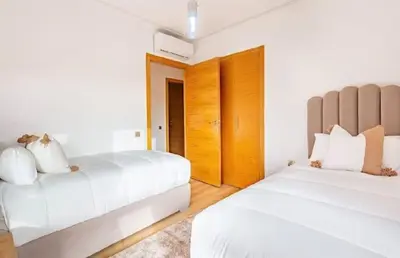 a white bedroom with two beds and wooden cabinets at Prestigia Golf Resort Luxury in Marrakech