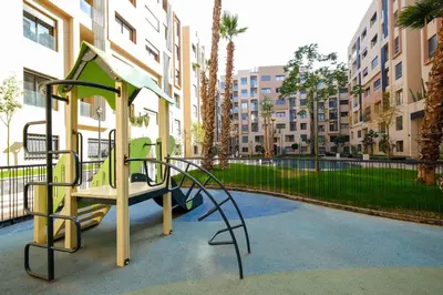 a playground in front of a building with palm trees at Appartement vacances famille Marrakech in Marrakech