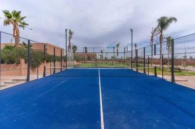 a tennis court with a net and palm trees at Luxury Villa with Breakfast & Padel Access in Marrakech