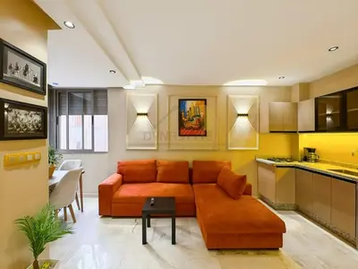a living room with an orange couch and a kitchen at Appartement neuf et chic Proche gare et CTM in Marrakech