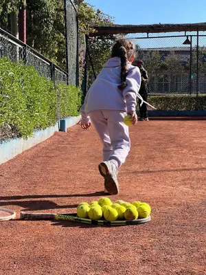 a woman running past a pile of tennis balls on a court at Fekhara CC in Marrakech