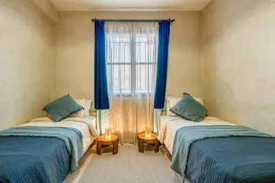 a room with two beds and a window with blue curtains at Beautiful Moroccan 2BR Close to City Center in Marrakech