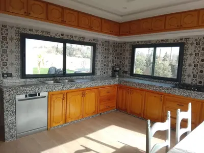 a kitchen with wooden cabinets and two windows at Alexandra Nomade - Maison de transition & séjours de répit in Marrakech