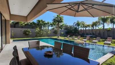 a swimming pool with chairs and an umbrella at Syrine Villa with temperate pool, not overlooked in Marrakech