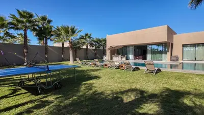 a ping pong table and chairs in front of a house at Syrine Villa with temperate pool, not overlooked in Marrakech
