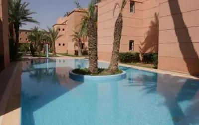a swimming pool with two palm trees in front of a building at Beautiful modern triplex in Qariya Sayhia in Marrakech