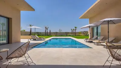 a pool with chairs and umbrellas next to a house at Villa Nour heated pool not overlooked in Marrakech