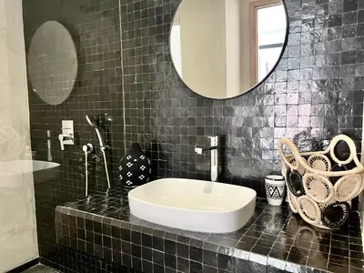 a black tiled bathroom with a sink and a mirror at Villa Bohō - 4 suites in El Rhechat