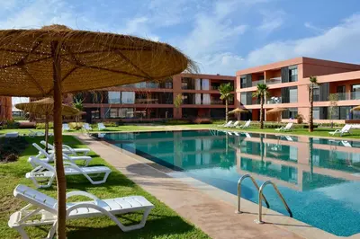 a resort swimming pool with chairs and an umbrella at Marrakech Luxury 2BR Pool View and Terrace for Remote Work in Marrakech