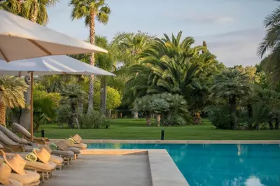 a pool with chairs and an umbrella and palm trees at Villa Primerose in Marrakech