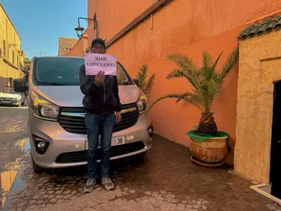 a woman holding a sign in front of a van at Riad Lapis-lazuli in Marrakech