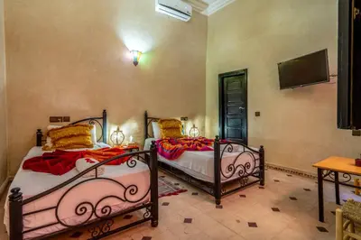 a bedroom with two beds and a tv on the wall at Riad Haj Thami in Marrakech