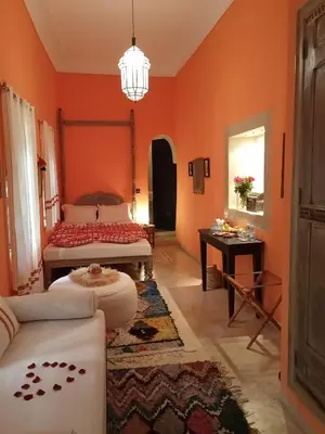 a living room with orange walls and a bed and a table at Dar al Sultan in Marrakech