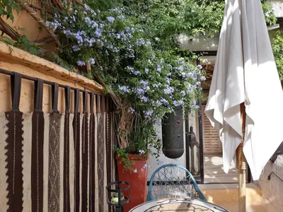 a patio with a table and a white umbrella and purple flowers at Riad Dar Oulhoum in Marrakech