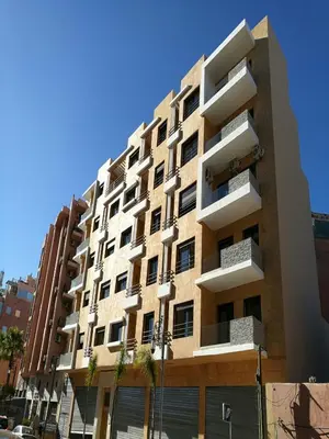 a tall apartment building with palm trees in front of it at Appartement Nour Guéliz Marrakech in Marrakech