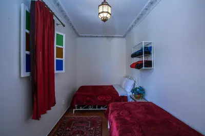 two beds in a room with red curtains and a lamp at Hotel Zitoune in Marrakech
