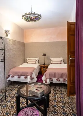 a bedroom with two beds and a table and a chandelier at Riad Zayane Atlas in Marrakech