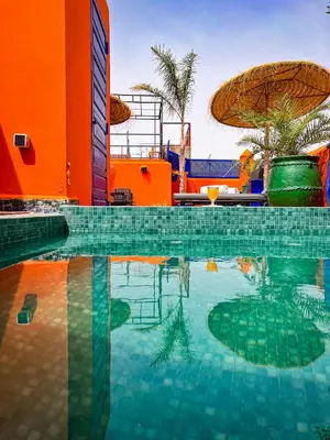 a swimming pool with an orange building and an umbrella at Riad Le Jardin de Lea, Suites & Spa in Marrakech